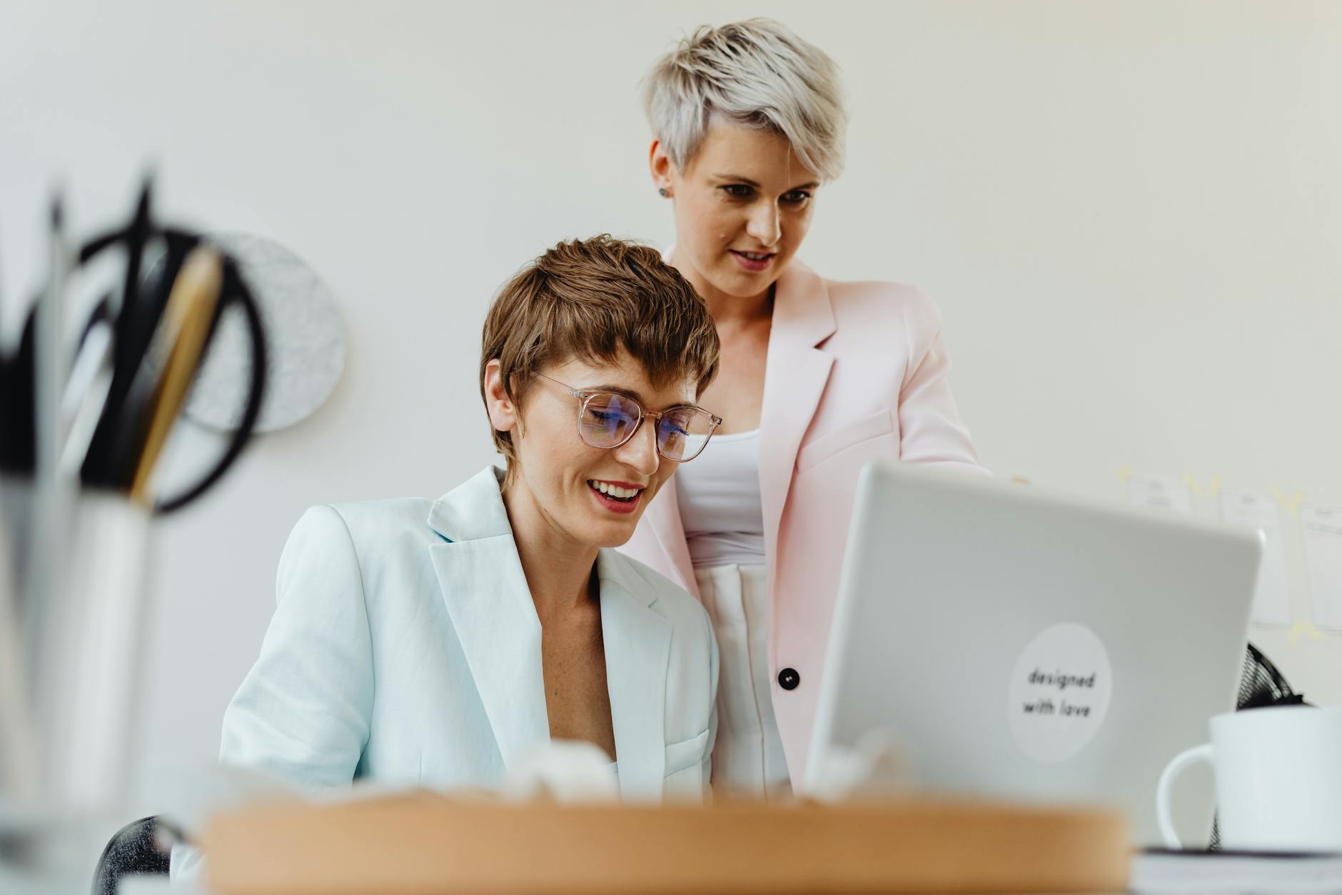 Zwei Frauen arbeiten glücklich an einem Laptop in einem hellen Büro